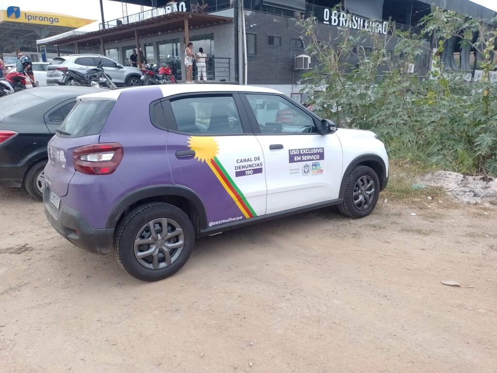 eículo branco da Secretaria da Mulher de Pernambuco estacionado, exibindo a bandeira de Pernambuco com a cor azul substituída pelo roxo.