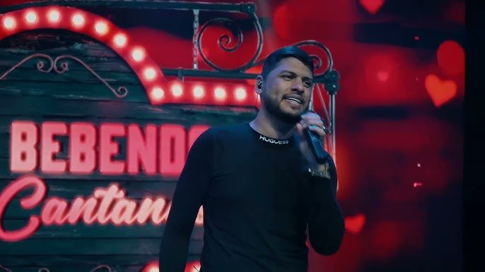 Cantor Rogério Som se apresentando em palco com iluminação vermelha durante show em Gravatá.