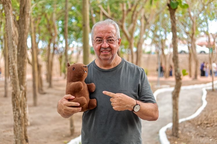 Prefeito Joselito Gomes sorrindo e segurando uma capivara de pelúcia durante a inauguração do Bosque das Capivaras em Gravatá, simbolizando a proteção animal.
