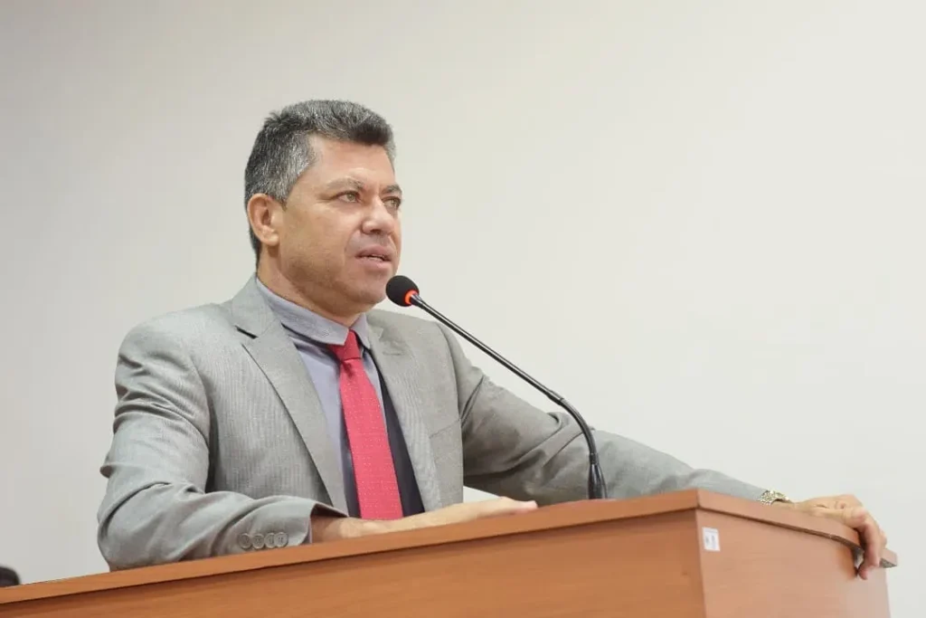 Vereador Ademir Batista em pronunciamento na Câmara de Chã Grande. Ele veste terno e gravata, está com as mãos apoiadas sobre o púlpito e fala ao microfone, mantendo uma postura solene em foto que ilustra a a cobrança pela manutenção da rodovia PE-71.