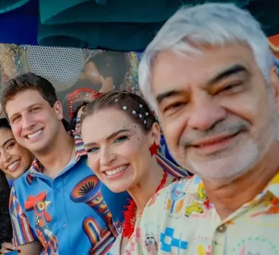 João Campos, Humberto Costa e Marília Arraes posam juntos e sorridentes em camarote no Carnaval de 2026. Os três estão vestidos com roupas de estampas florais e tropicais. A imagem captura a união política da Frente Popular em Pernambuco durante a folia, com Humberto Costa à esquerda, João Campos ao centro e Marília Arraes à direita, todos olhando para a câmera e fazendo pose para fotos.