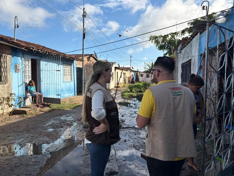 Equipes técnicas da Secretaria de Assistência Social e Juventude de Gravatá realizam atendimento domiciliar e cadastramento de famílias na Rua da Linha, Área Verde, após forte chuva no município. Profissionais uniformizados ou identificados conversam com moradores em área afetada.