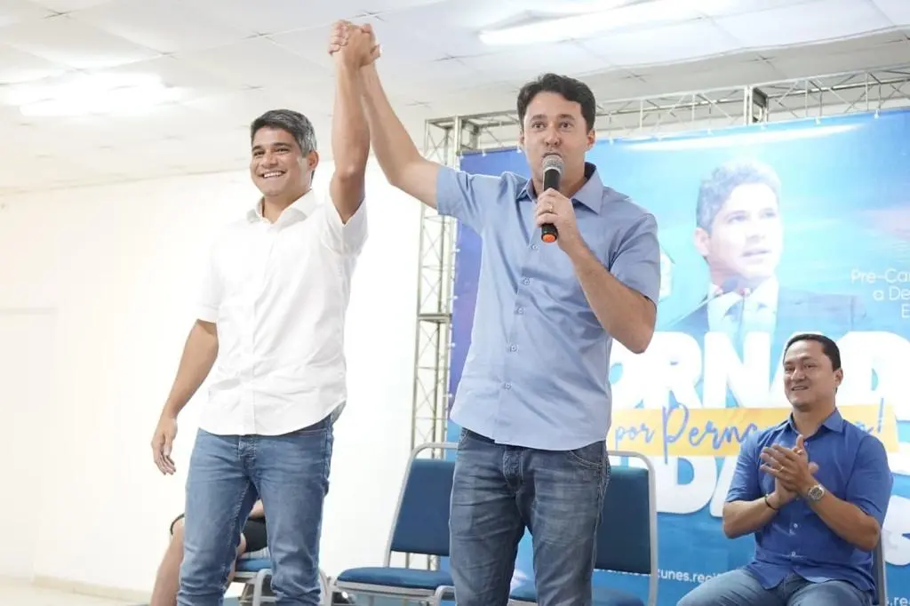 Anderson Ferreira, presidente estadual do PL, levanta o braço de Renato Antunes em ato de filiação ao partido. O deputado federal André Ferreira aparece ao fundo e um telão exibe a foto de Antunes em segundo plano.