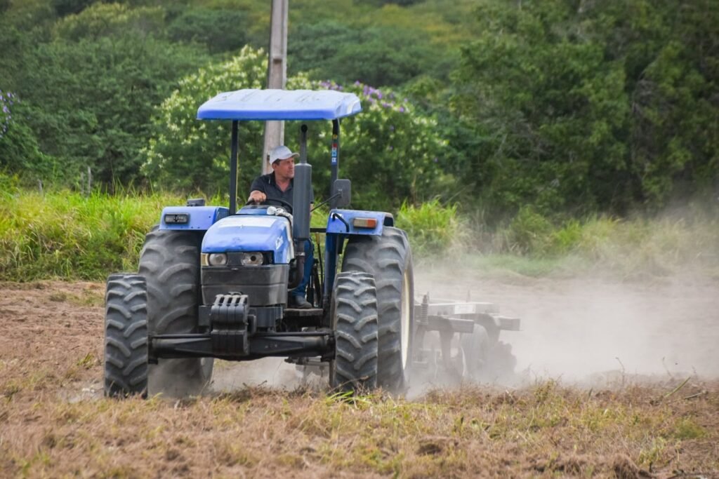 Trator azul realizando serviço de aração de terra para agricultura familiar em zona rural de Gravatá.