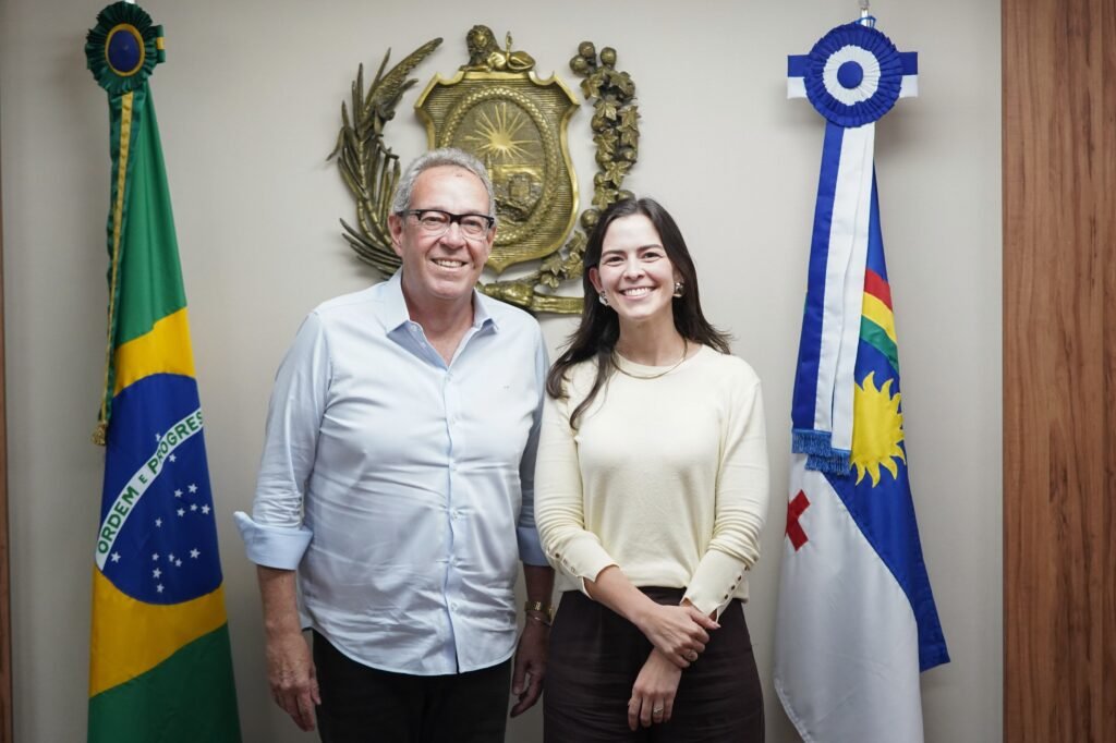 O presidente da Alepe, Álvaro Porto, e a deputada federal Maria Arraes sorriem lado a lado entre as bandeiras do Brasil e de Pernambuco, no gabinete da presidência da Assembleia Legislativa.