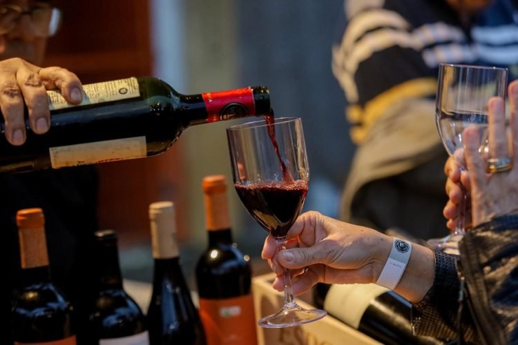 Pessoa servindo vinho tinto em uma taça durante o Festival de Queijos e Vinhos no Tardes no Polo em Gravatá.