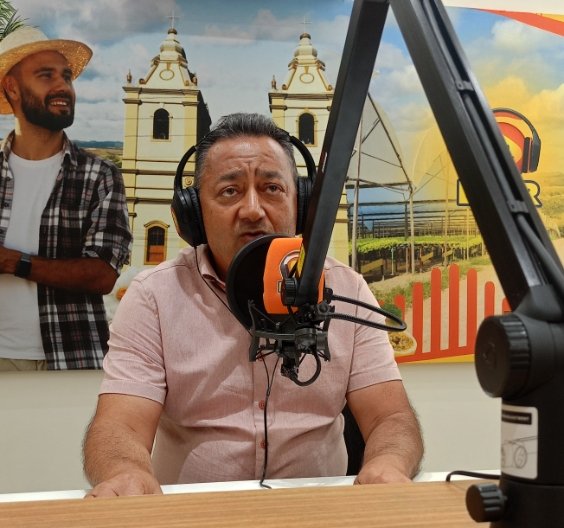 Lula do Padre em estúdio de rádio usando fones de ouvido e falando ao microfone da Líder FM.