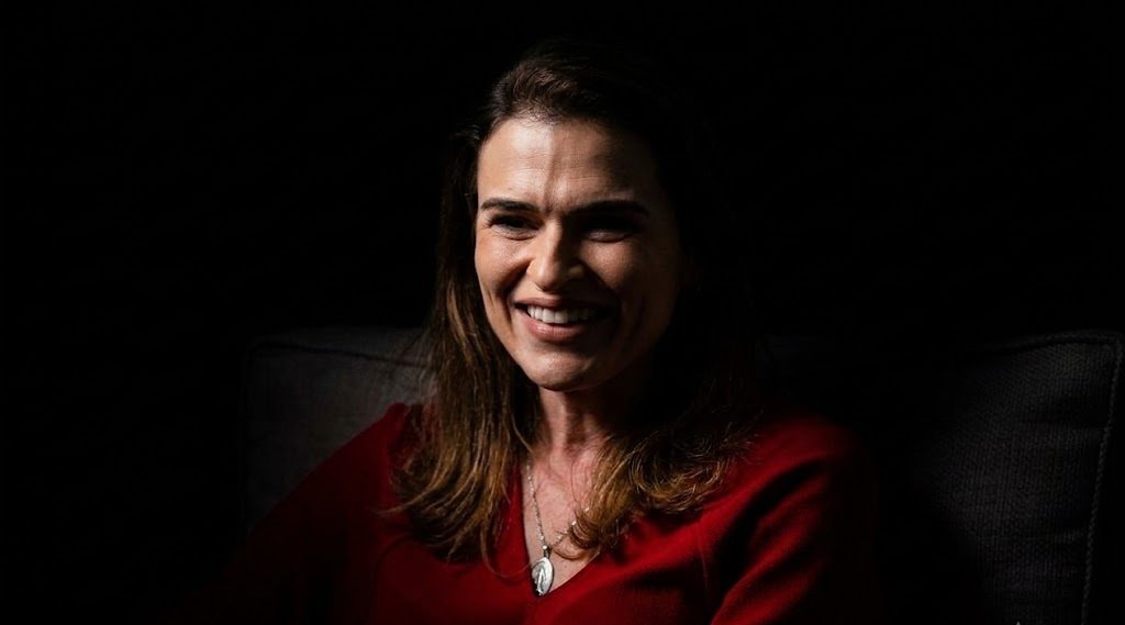 Marília Arraes (PDT), candidata ao Senado em Pernambuco, sorri em fundo escuro com iluminação dramática estilo chiaroscuro e blusa vermelha.