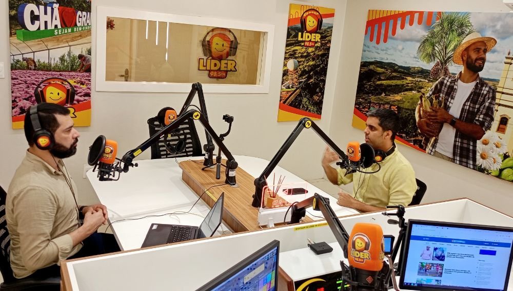 Renan Hallais concede entrevista ao vivo a Ismael Alves no estúdio da Rádio Líder FM, em Chã Grande, Pernambuco. Ambos estão sentados em uma mesa de transmissão equipada com microfones e fones de ouvido.