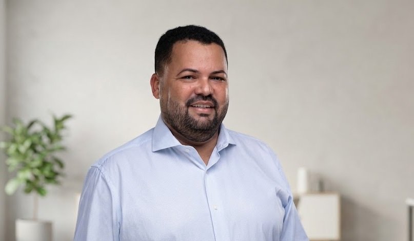 O vereador de Vitória de Santo Antão Josias Alves da Silva sorri vestindo camisa social azul clara em ambiente de escritório corporativo.