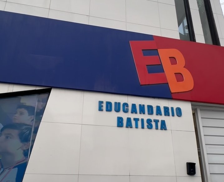 Fachada da escola Educandário Batista em Chã Grande, exibindo placa azul e vermelha com logotipo EB e letras azuis na parede branca.