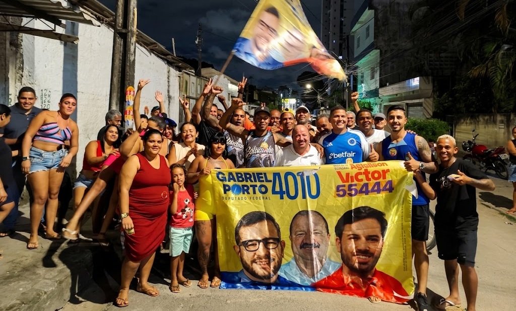 Nilson Pereira com grande grupo de apoiadores e banner de campanha de Gabriel Porto e Aglailson Victor em rua no Recife à noite. No banner, "GABRIEL PORTO 4010" e "AGLAILSON VICTOR 55444".