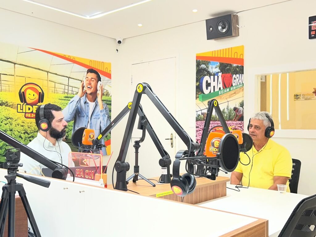O ex-prefeito de Amaraji, Jânio Gouveia, de camisa amarela, e o apresentador Ismael Alves, usando fone de ouvido, no estúdio da Rádio Líder FM durante o programa Panorama Político.