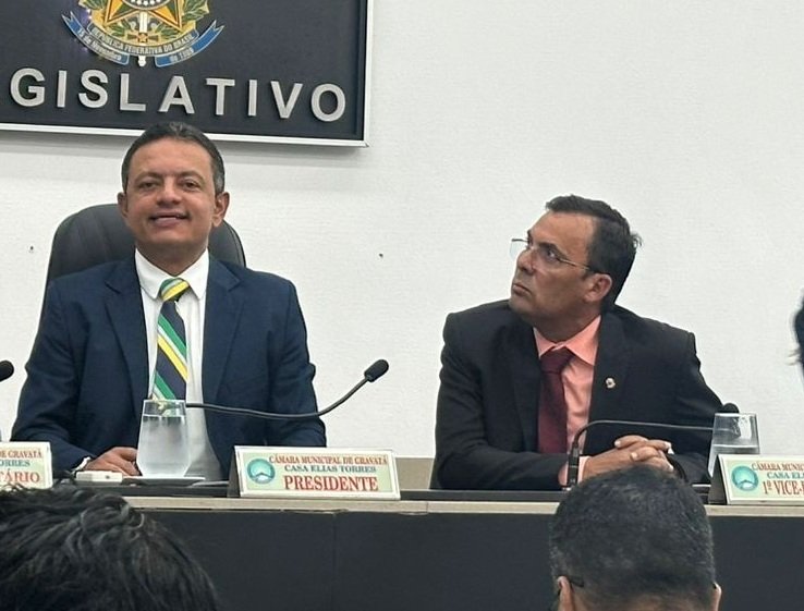 Fotografia da Mesa Diretora da Câmara Municipal de Gravatá com dois homens, identificados pelas placas de identificação como Léo do Ar e o 1º Vice-Presidente. No fundo, lê-se "LEGISLATIVO" com o brasão da República Federativa do Brasil acima.