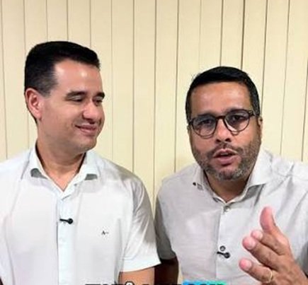 O deputado estadual Joaquim Lira, à esquerda, sorri e olha para o vereador Rafael Prequé, à direita, que veste óculos de armação escura e gesticula enquanto fala. Ambos vestem camisas sociais claras em ambiente com painel ripado de fundo.