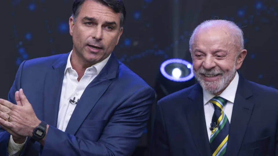 Flávio Bolsonaro e Lula durante debate político na televisão, em cenário com iluminação azul.