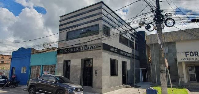 Fachada do prédio do Poder Legislativo e Anexo I da Câmara Municipal de Ribeirão, revestido em granito cinza, sob céu ensolarado e com fiação elétrica visível.