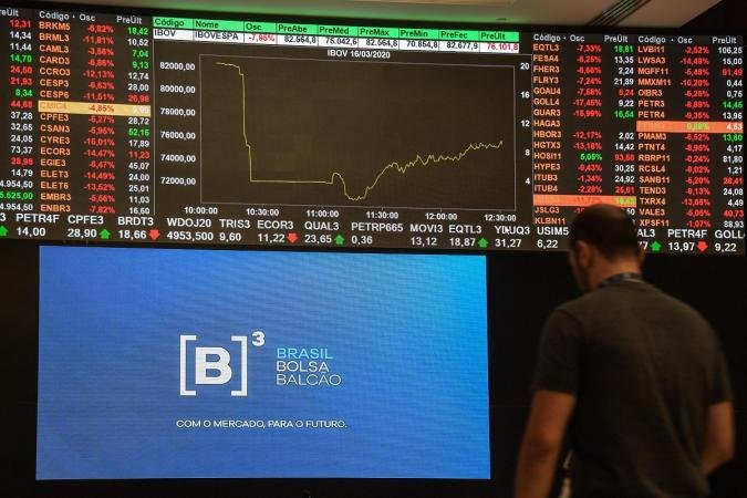 Homem de costas observa um painel eletrônico com cotações da bolsa de valores e o logotipo da B3 (Brasil, Bolsa, Balcão) iluminado em azul, ilustrando a reação positiva do mercado financeiro após o primeiro turno das eleições de 2026.