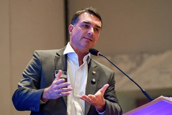 Político de terno cinza discursa ao microfone durante evento.