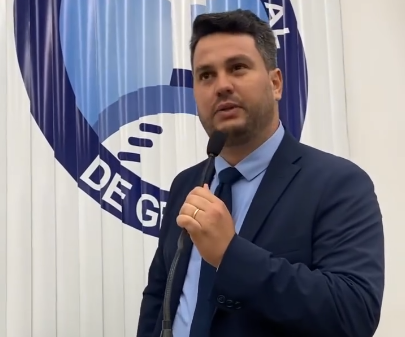 Vereador Tadeuzinho (Avante) vestindo paletó azul-marinho e gravata azul-escura, segurando um microfone e discursando na Câmara Municipal de Gravatá. Ao fundo, lê-se parte do brasão oficial da Casa Legislativa.