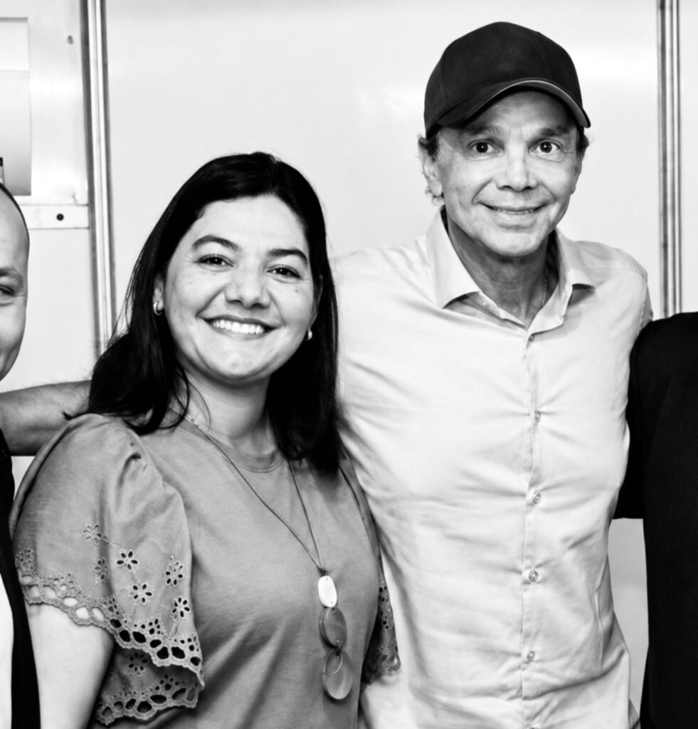 Fotografia em preto e branco de Viviane Facundes, primeira-dama de Gravatá, sorrindo ao lado do cantor Netinho, que usa boné e camisa de botão, durante evento em Gravatá em 2022.